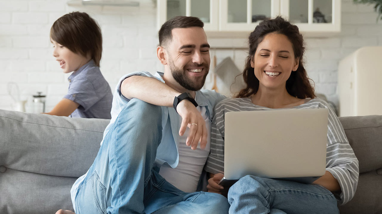Un couple devant un ordinateur pendant qu'un enfant joue derrière