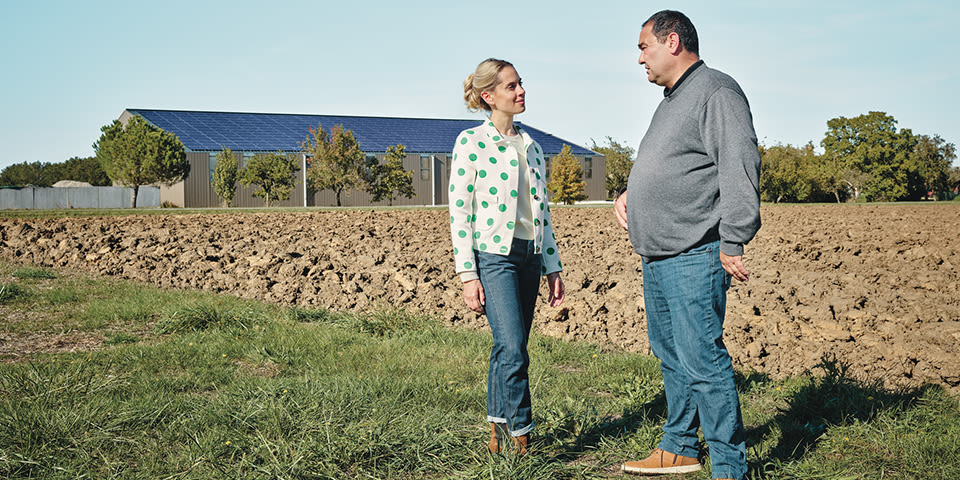 Cerise discute avec un agriculteur devant un bâtiment de la ferme avec un toit en panneaux photovoltaïques.