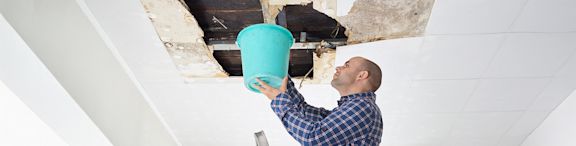 Un homme avec un seau à cause d'un dégât des eaux à son plafond.
